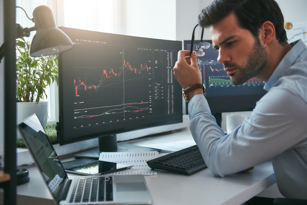 good looking day trader holding his glasses to get a better look at his small laptop screen trying to focus on analyzing the stock or charts